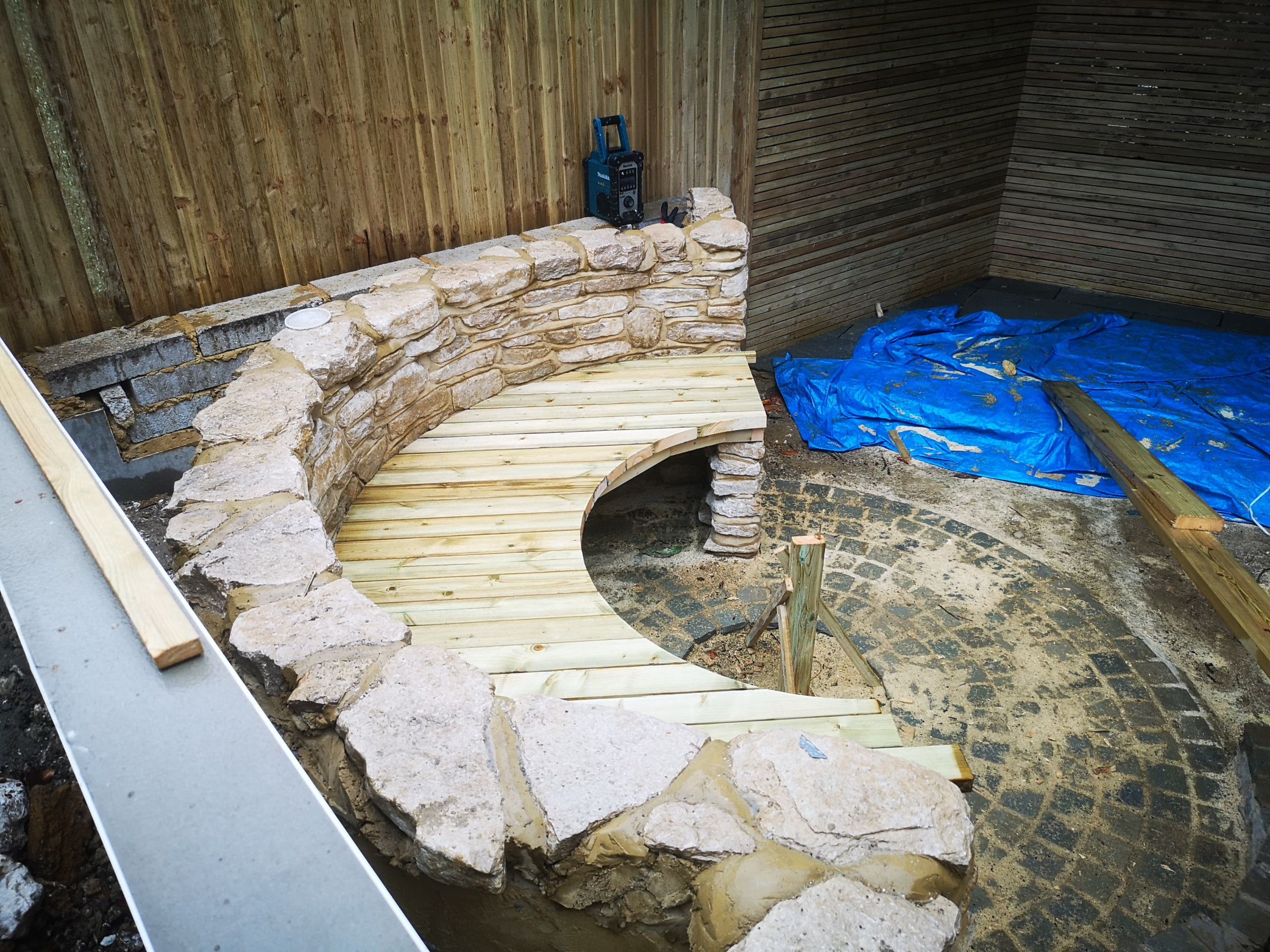 Construction of curved timber garden seating around a stone wall